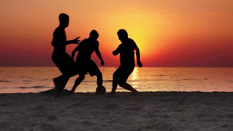 4k Silhouette of three guys playing football on the beach at sunset