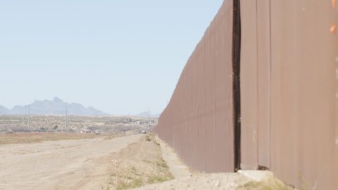 A pan shot looking at the length of the fence on the US and Mexico border on a sunny afternoon.