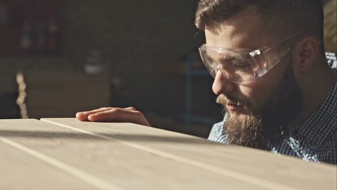 A young bearded carpenter checks the quality of the boards in the sun. RAW video record.
