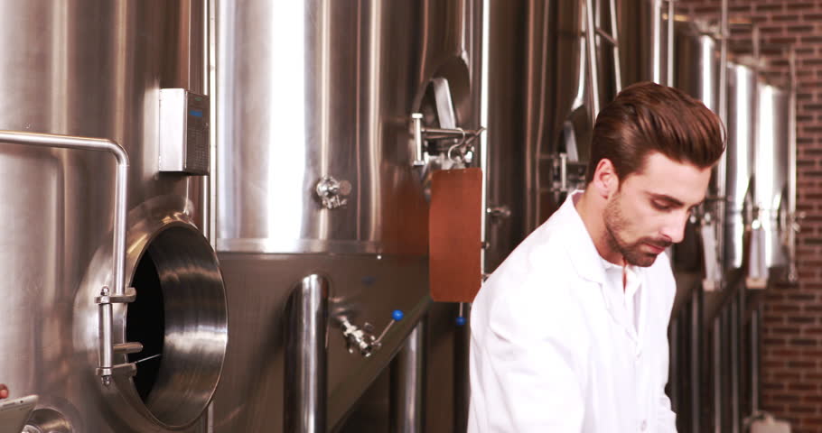 Focused scientist looking beaker with beer in the factory