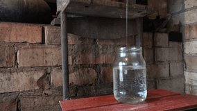 tilt up of pure fresh liquid alcohol flow in glass pot in rural kitchen indoor. 4K UHD video clip.