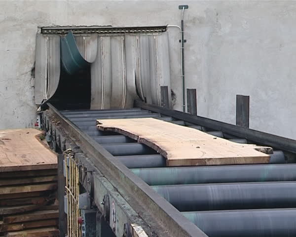 Boards moving on escalator from outside to sawmill. Pile of boards.  