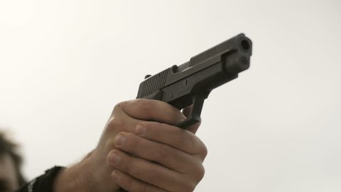 Slow motion close-up shot of hands shooting several bullets from a handgun.