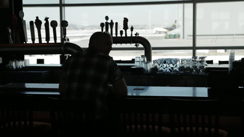 A silhouette of a guy in a bar receiving a drink and taking a sip. Shot at an airport.