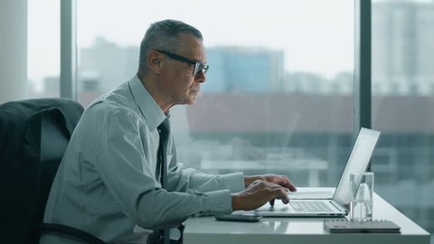 elderly businessman look at phone and working with computer in modern office