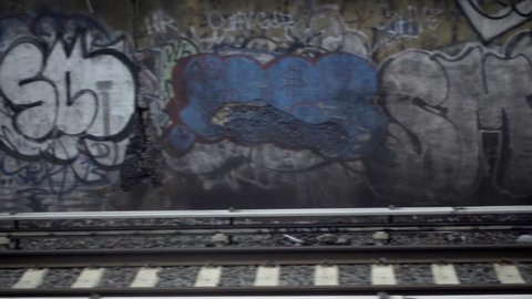 graffiti on wall passing from moving subway train view above gritty tracks in NYC slow motion