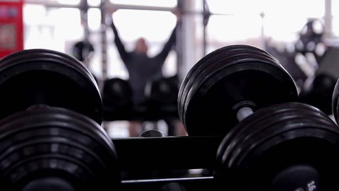 Defocused silhouette of male athlete doing bench press exercise in the gym