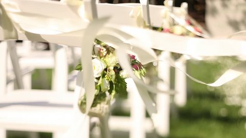 Wedding decor on the chairs , ribbons and flower on white chairs , roses and wild flowers in small vases in the wedding decor , satin ribbons are developed in the wind
