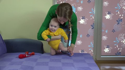 Beautiful mother with her infant baby son boy make stand up exercise on bed. Special exercises for newborn health. video clip.