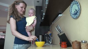 Careful woman hold her baby daughter on hands and feed with spoon in kitchen at home. Infant girl eating food mash. Static shot. video clip.