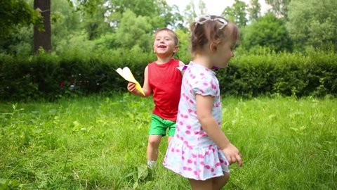 Little cute girl and boy play with paper airplanes in summer park