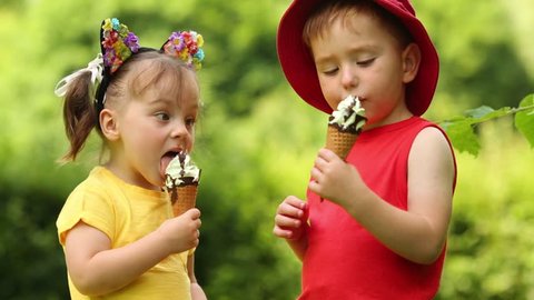 Cute little boy and girl eat sweet ice cream in green park