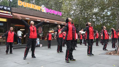 SHANGHAI, CHINA - 4 NOVEMBER 2015: People do morning dance exercises to stay fit and healthy, a Dunkin Donut store in the background makes for an interesting contrast, Shanghai, China