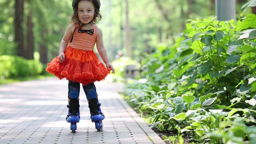 Little girl in skirt and roller-blades poses in park