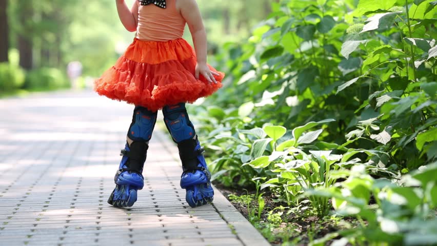 Legs of little girl in skirt roller-blading in park