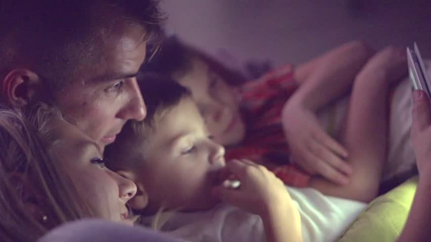 Happy family- Father, mother and Two kids lying down on the sofa and using tablet pc at night. Family watching movie on tablet computer in a dark room. HD 1080p, slow motion 240 fps, high speed camera | Shutterstock HD Video #14842069