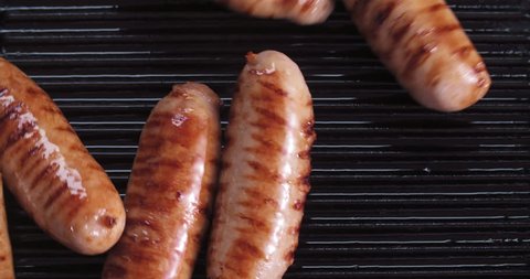delicious grilled pork sausages rollin on hot grill pan from overhead in 4K slow motion