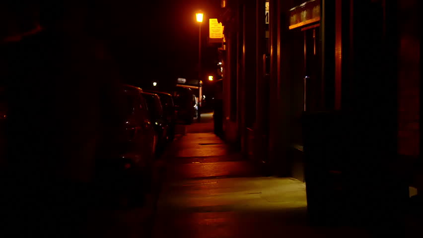 slow motion of a man running on a dark sidewalk to escape from followers