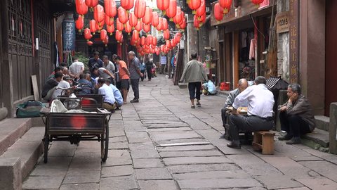 FENGHUANG - 19 SEPTEMBER 2015: Classic scene in China, people play traditional Chinese chess in a narrow alley in Fenghuang. A motorbike drives by marking the contrast between modern and traditional.