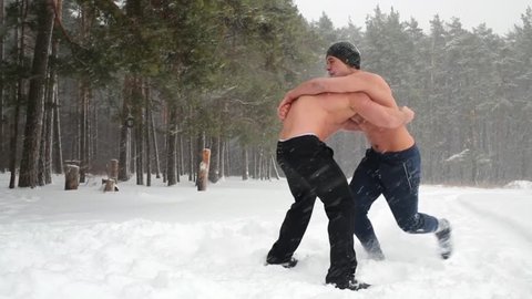 Two bare-chested guys wrestle standing at outdoor sportsground in winter wood.