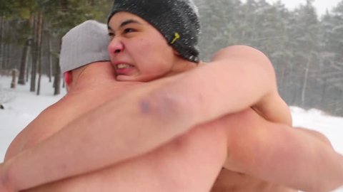 Closeup heads, shoulders and arms of two guys wrestling at sportsground in winter snowy wood.