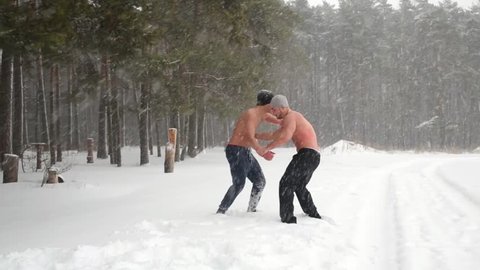 Two bare-chested guys wrestle practicing hip throw at outdoor sportsground in winter forest.