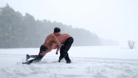 Two bare-chested guys wrestle practicing holding at outdoor sportsground in winter forest.