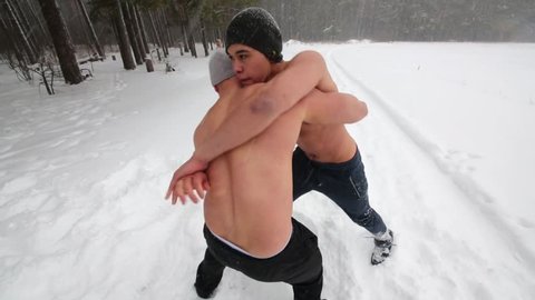 Two bare-chested guys wrestle standing at outdoor sportsground in winter forest.