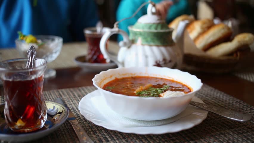 Plate of borsch with sour cream, tea in glasses, teapot and buns on table at cafe. | Shutterstock HD Video #14866402