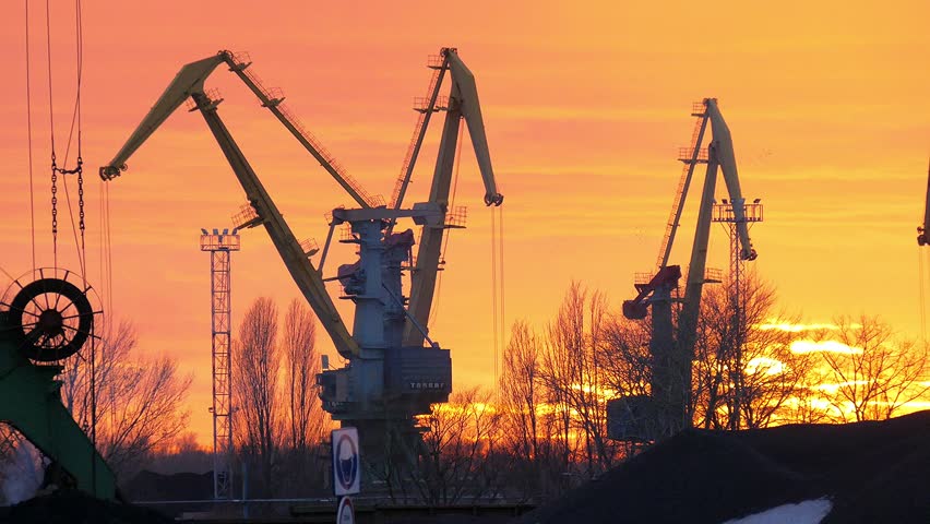 Winter sunset and working cranes in the port.