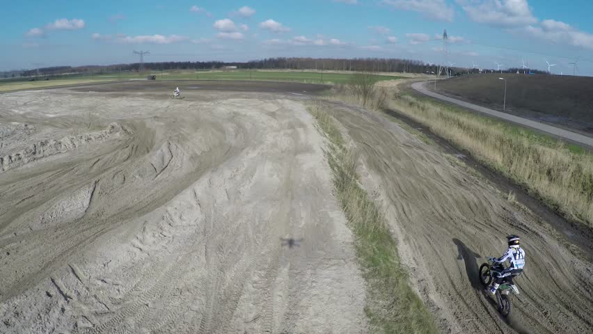 Aerial of motocross dirt track drone following motorcross rider off-road motorcycle racing held on enclosed off-road circuit with serveral corners and jumps driving through sand mud and dirt 4k