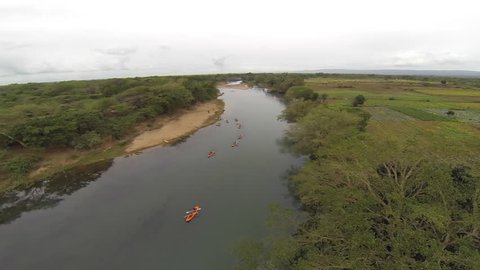 Panoramic aerial of ten canoes rowing down the African Pongola River with crops on the right bank and bush-veld on the left side.