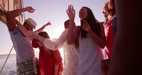 Group of friends of mixed races dancing and drinking together at a party on a yach at sunset with soft evening sunflare in Slow Motion