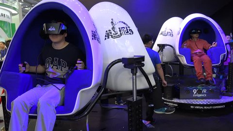 SHENZHEN, CHINA - 20 NOVEMBER 2015: People sit in moving egg shaped chairs, while wearing virtual reality glasses, at a trade show in Shenzhen, China
