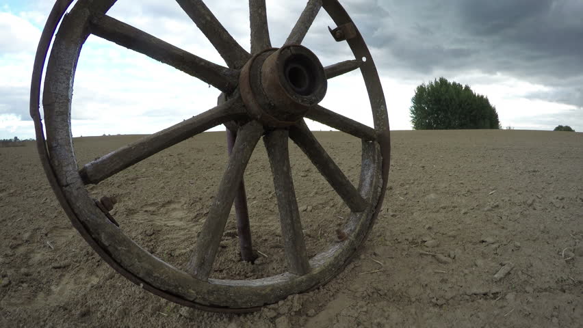 Old wooden wheel in freshly plowed clay soil field on overcast day, time lapse 4K

