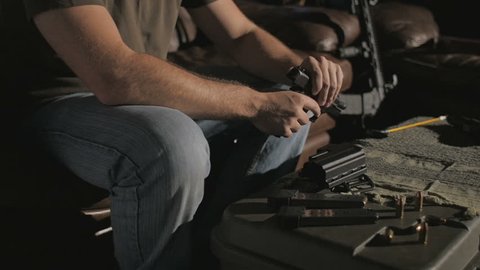 Shot of a man sitting on a couch. He takes the clip out of a .45 caliber handgun, disassembles the gun, then begins cleaning it.