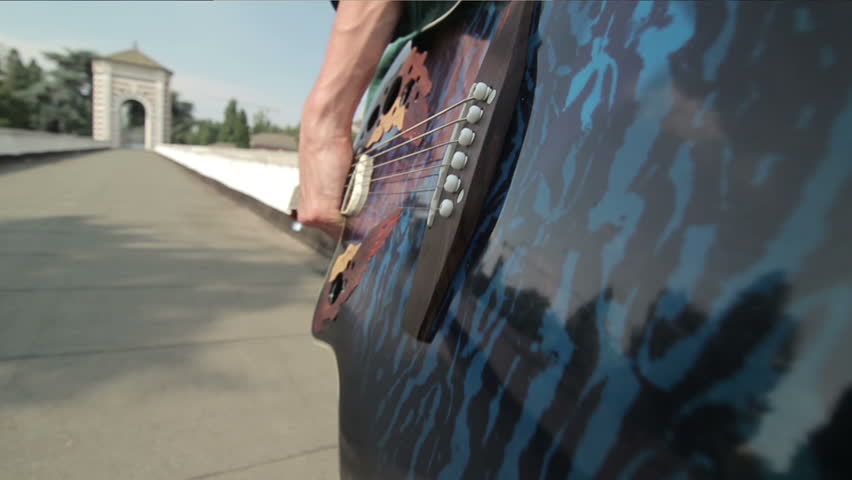 A young man with a guitar walking, steadicam shot