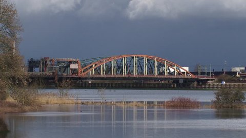 ZUTPHEN, THE NETHERLANDS - MARCH 2016: IJssel bridge, urban traffic and passenger train crossing the bridge. Moving shadow, threatening sky.