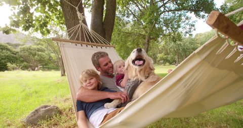 Modern father relaxing and enjoying quality time with his two blonde sons and labrador dog outside in hammock in Slow Motion