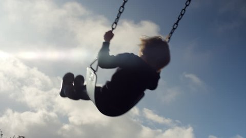 A little girl swinging, slow motion, silhouette in the sky, lens flare