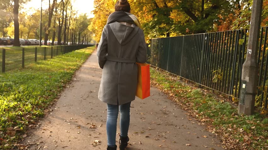 Beautiful young girl with shopping bag walking in park. Autumn time.