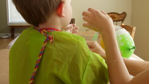 A mother and her boy make a piñata with a balloon, paper, and paste dolly shot