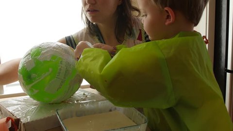 A mother and her boy make a piñata with a balloon, paper, and paste dolly shot