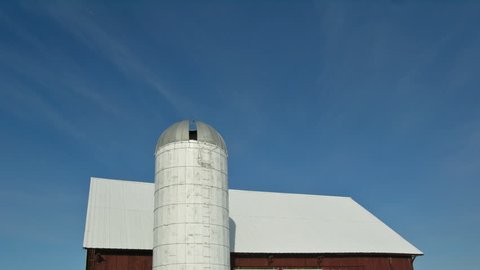 timelapse clip of a windmill shadow traveling accross a silo and barn