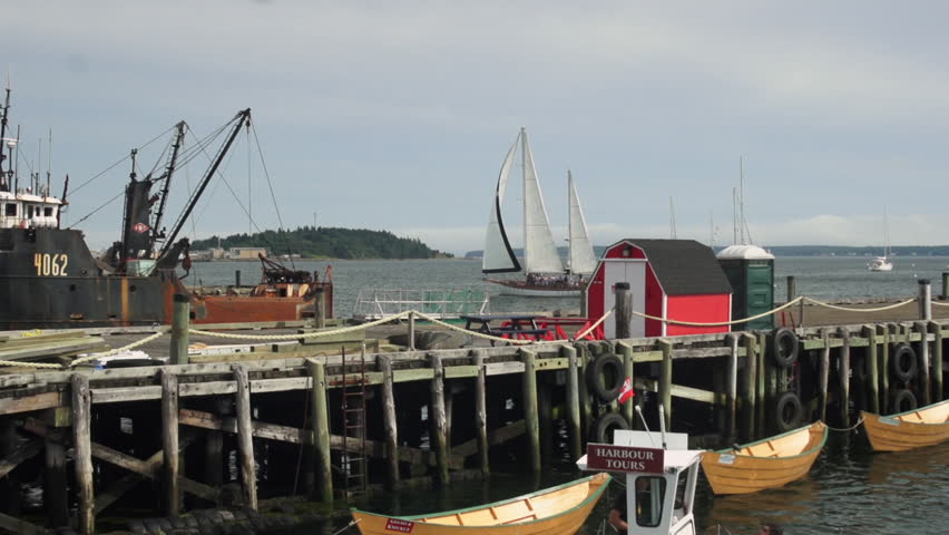 A large deep sea fishing trawler arrives at the docks in Lunenburg Harbour in Nova Scotia. Small wooden dories float against a wooden pier in the foreground of this World Heritage Site.