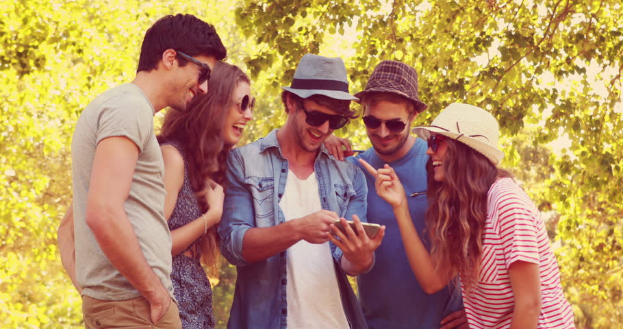 Happy friends watching photos on a smartphone in the park on a sunny day