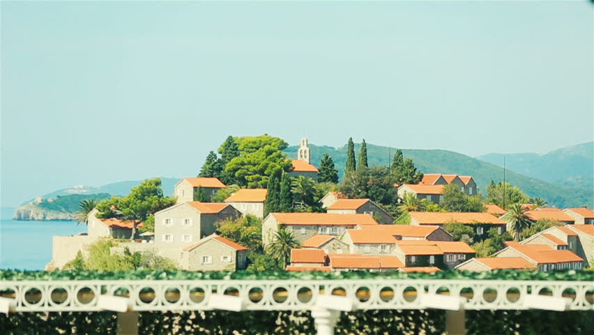 Silhouette of charming bride in white robe standing on terrace and  enjoying the view of Sveti Stefan in Montenegro, Budva