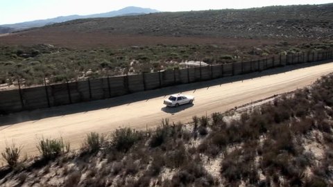 A car drives along a road bordered by a high fence.