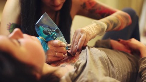 Cinemagraph loop - Young girl tattoo artist working on a tattoo for a girl on her chest - motion photo Adlı Stok Video