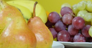 Beautiful dolly shot on left, pears on plate close up, different kinds of fruits on table, from pears to oranges close up, grapes and other fruits in background, no color grading, raw video, 24fps, 4K